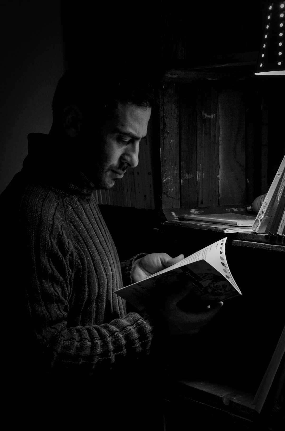 Studio portrait of a Croatian man in his fifties with grey hair and a warm cardigan sitting in his home study surrounded by bookshelves