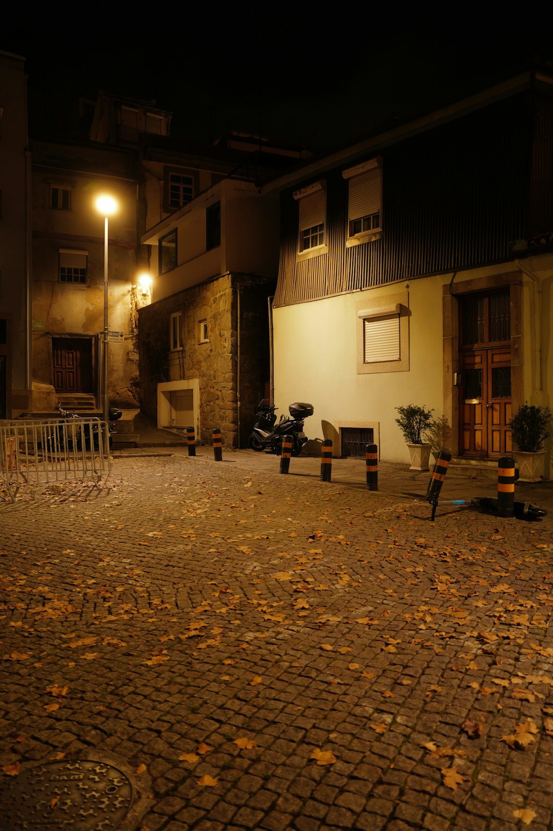 Foggy old European town street at night with a glowing streetlamp and wet cobblestones